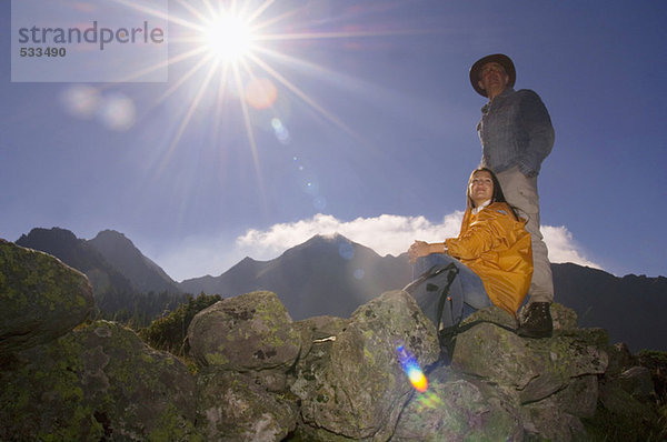 Paar in den Bergen  Mann stehend  Frau auf Felsen sitzend
