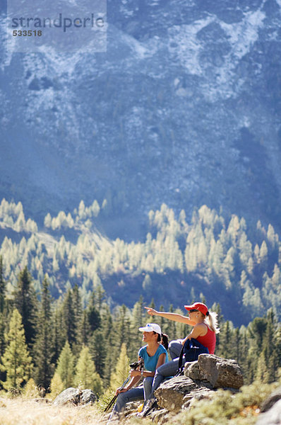 Zwei Frauen sitzen auf einem Felsen in den Bergen  Seitenansicht
