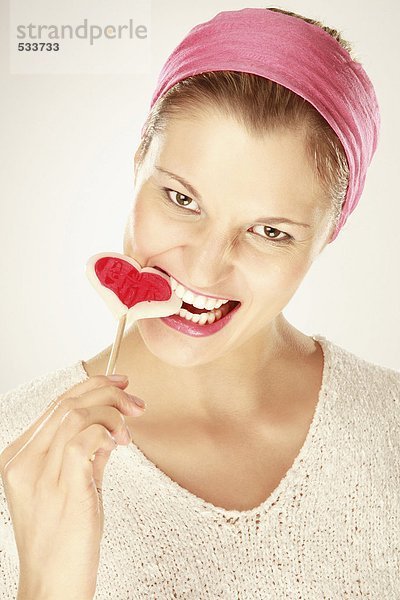 Junge Frau isst herzförmigen Lolli  Nahaufnahme  Portrait