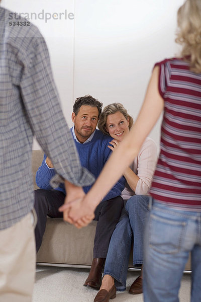 Teenage couple holding hands  parents sitting on sofa