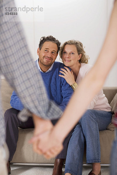 Teenage couple holding hands  parents sitting on sofa