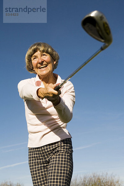 Senior Frau schwingt Golfschläger  lächelnd  niedriger Blickwinkel