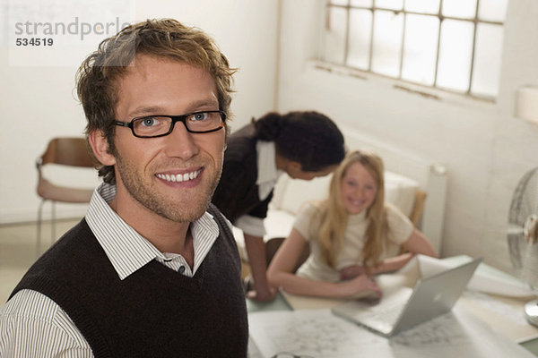 Junger Mann lächelnd  Frauen mit Laptop im Hintergrund