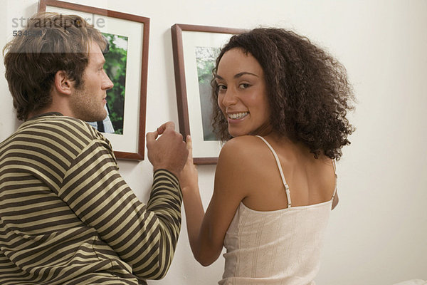 Junges Paar hängt Bilderrahmen auf  Frau lächelt