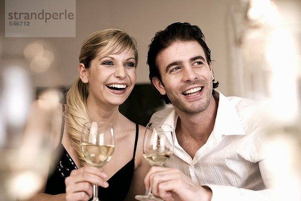 Lachendes Junges Paar mit Weissweinglläsern in der Hand