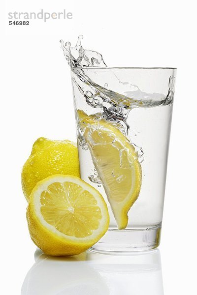 Eine Zitronenspalte fällt in ein Glas Wasser