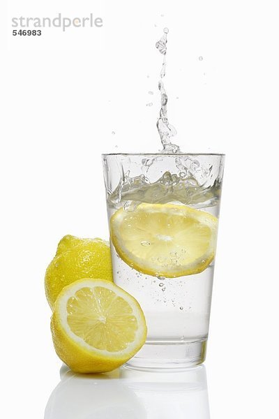 Eine Zitronensscheibe fällt in ein Glas Wasser