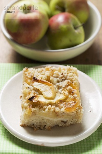 Stück Apfel-Streusel-Kuchen  frische Äpfel im Hintergrund