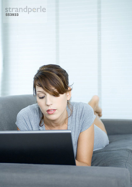 Junge Frau auf der Couch liegend  mit Laptop