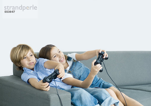 Junge und Mädchen spielen Videospiel  halten Joysticks auf dem Sofa aus.