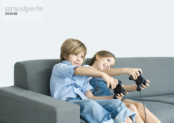 Junge und Mädchen spielen Videospiel  halten Joysticks auf dem Sofa aus.