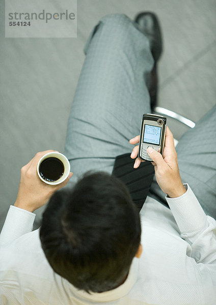 Geschäftsmann mit Smartphone  der eine Tasse Kaffee hält.