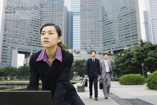 Geschäftsfrau mit Laptop im Büropark  zwei Geschäftsleute im Hintergrund