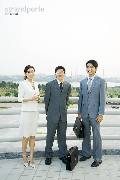 Drei Geschäftsleute stehen am Geländer  schauen in die Kamera  Ganzkörperporträt