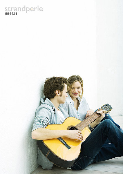 Junges Paar auf dem Boden sitzend  Mann spielt Gitarre
