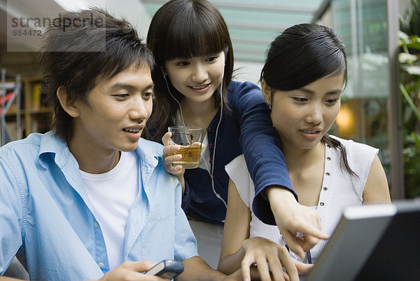 Drei junge Erwachsene mit dem Laptop  einer zeigt auf den Bildschirm.