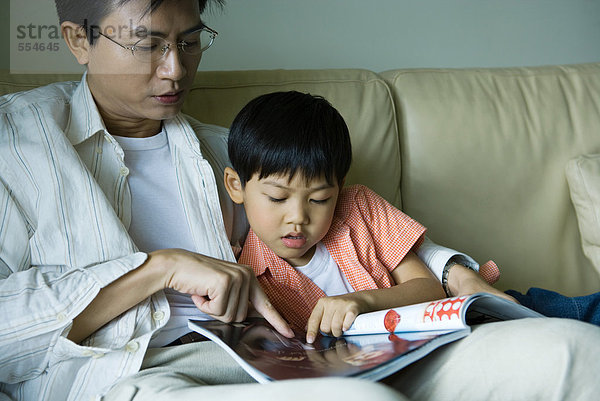Vater und Sohn sitzen auf dem Sofa und schauen sich die Zeitschrift an.