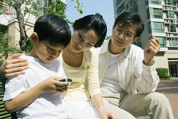Familie  Junge  der das Handy benutzt  während die Eltern zusehen.