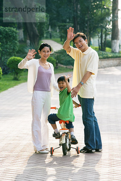 Junge auf dem Fahrrad  Eltern auf beiden Seiten  winkend vor der Kamera