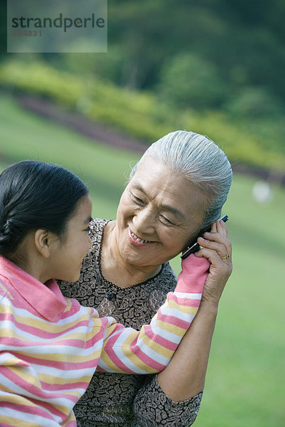 Mädchen mit Großmutter  hält Handy an Ohr