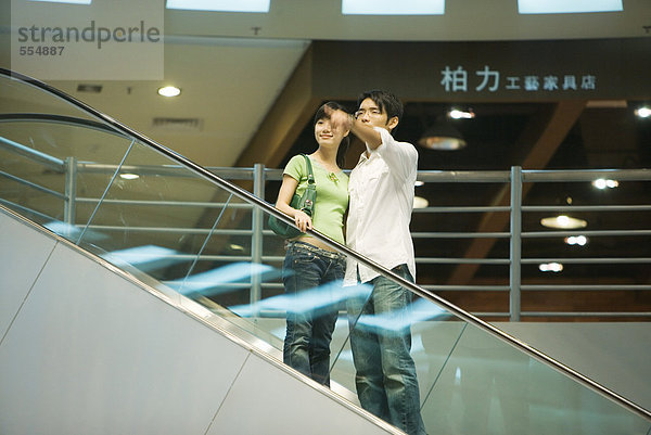 Ein Paar nimmt eine Rolltreppe im Einkaufszentrum  der Mann zeigt aus dem Rahmen.