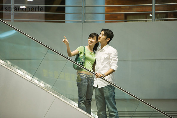 Paar  das Rolltreppe im Einkaufszentrum nimmt  Frau  die aus dem Rahmen zeigt