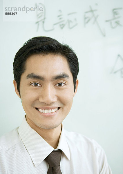 Geschäftsmann lächelnd  chinesische Schrift auf Whiteboard im Hintergrund  Portrait