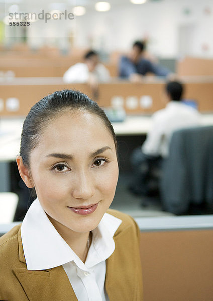 Geschäftsfrau lächelt vor der Kamera  Großraumbüro im Hintergrund
