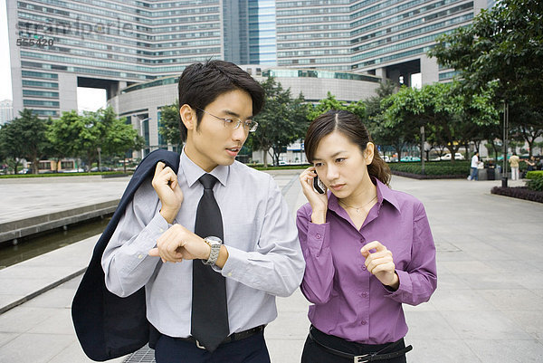 Zwei junge Geschäftsleute im Büropark  Frau mit Handy und Mann mit Armbanduhr