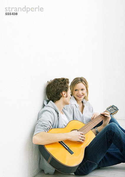 Junger Mann und Frau auf dem Boden sitzend  Mann spielt Gitarre