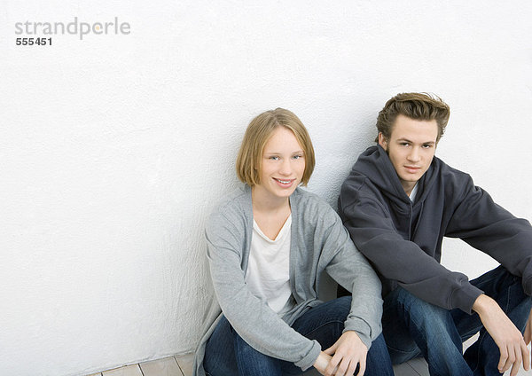 Junger Mann und Frau sitzen auf dem Boden und lehnen sich an die Wand.