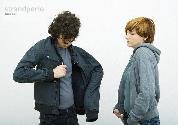 Junger Mann und Frau stehen  Mann zieht Jacke an  während die Frau zusieht.