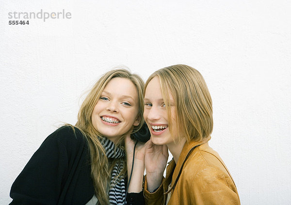Zwei junge Freundinnen teilen sich Kopfhörer und lächeln in die Kamera.