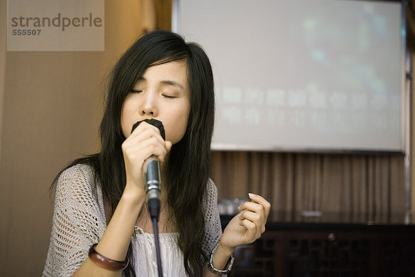 Junge Frau singt Karaoke  Augen zu.