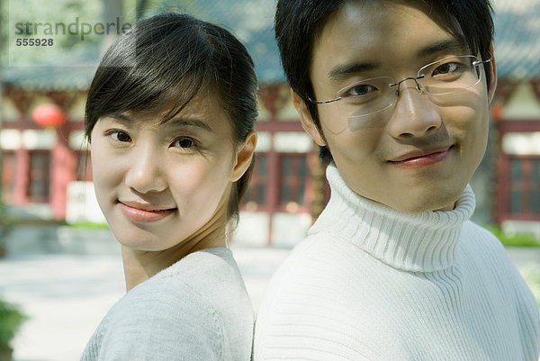 Paar Rücken an Rücken  lächelnd vor der Kamera  traditionelles chinesisches Gebäude im Hintergrund