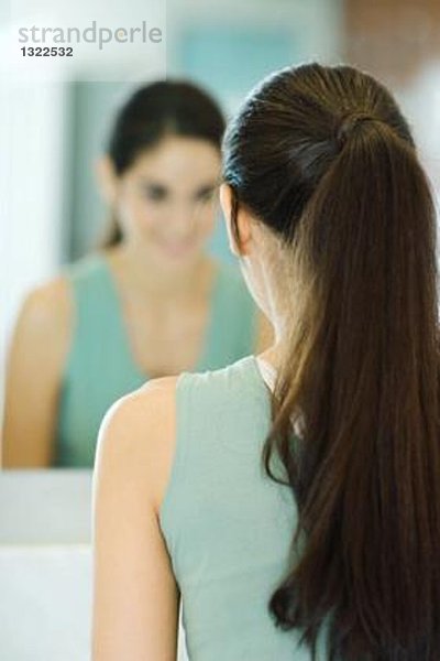 Frau schaut sich selbst im Spiegel an  Rückansicht