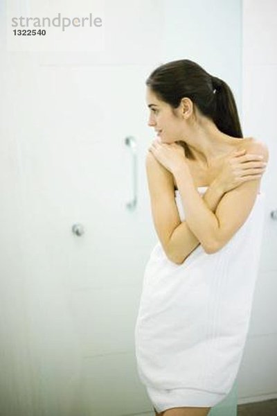 Frau stehend in Handtuch gewickelt  Hände auf den Schultern  wegschauend