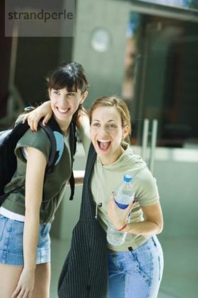 Zwei junge Frauen stehen zusammen  eine mit der Hand um die Schulter der anderen  halten eine Flasche Wasser und machen ein Gesicht.