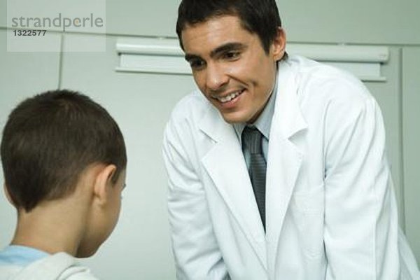 Arzt lehnt sich vor  lächelt den kleinen Jungen an.