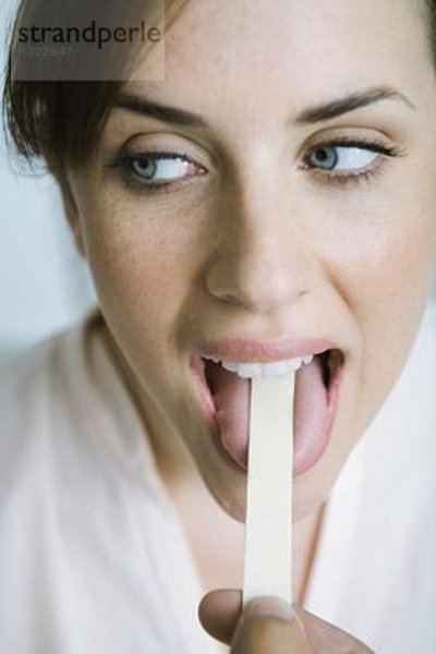 Frau mit niedergehaltener Zunge mit Zungenspatel