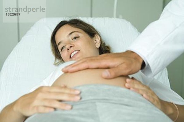 Schwangere Frau auf dem Rücken liegend  Arzthand auf dem Bauch