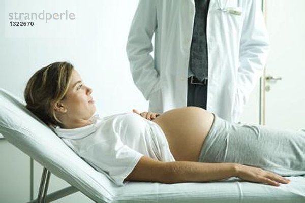 Schwangere Frau auf dem Rücken liegend  Arzt neben ihr stehend