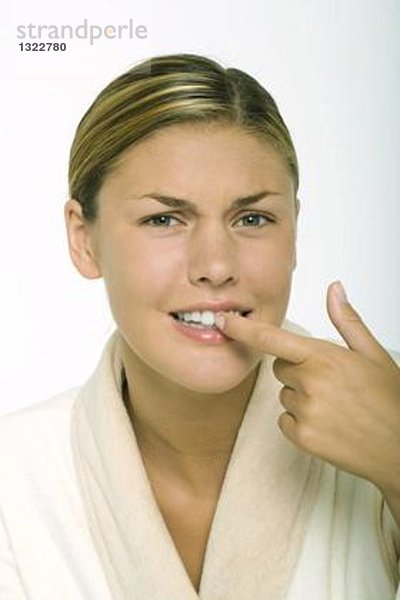 Junge Frau mit Bademantel  berührenden Zähnen und furchender Stirn
