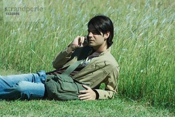 Mann im Gras liegend  mit dem Handy