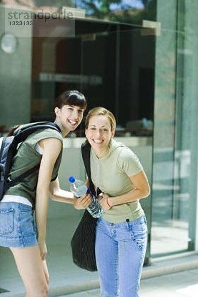 Zwei junge Frauen stehen draußen in Straßenkleidung und lächeln in die Kamera.