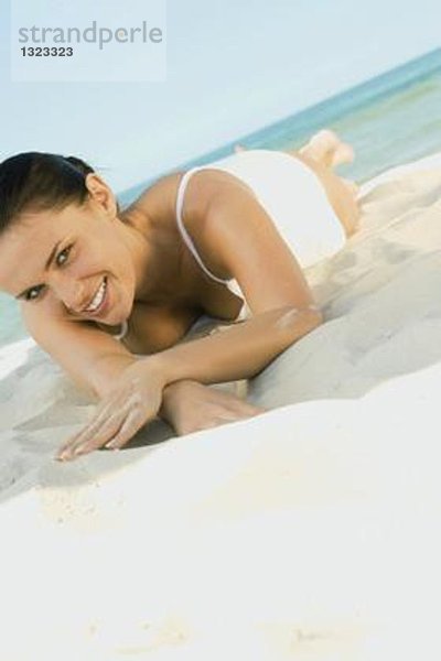 Frau auf Sand liegend  lächelnd vor der Kamera
