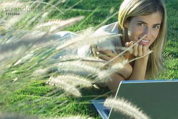 Junge Frau im Feld liegend mit Laptop