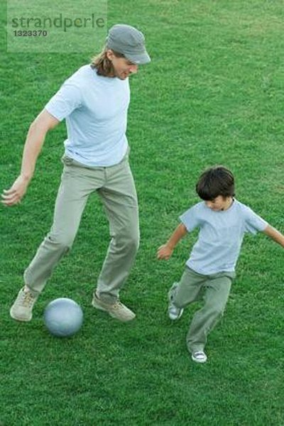 Mann und Junge spielen Fußball auf Rasen