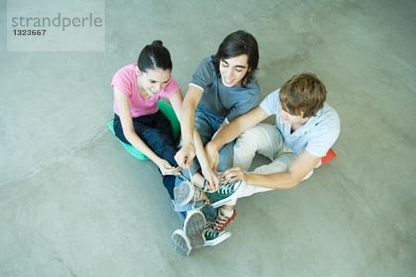 Teenager-Freunde mit Beinen an den Knöcheln  Schnürsenkel aus Leinenschuhen bindend