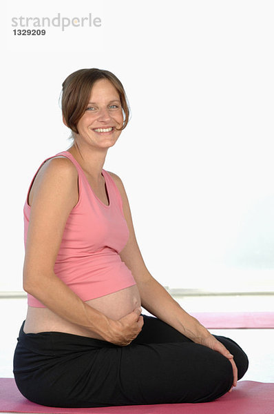 Schwangere Frau auf Yogamatte sitzend